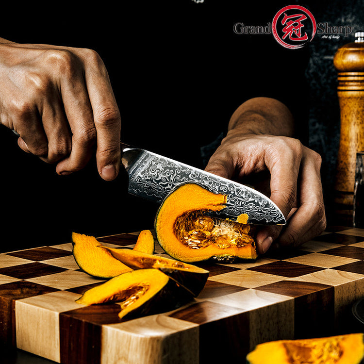 A chef’s hands using the Damara Chisai Damascus paring knife to precisely slice a small pumpkin on a cutting board.
