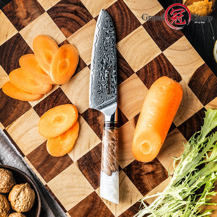 	The Damara Chisai Damascus paring knife resting on a cutting board with a sliced carrot, walnuts, and fresh greens.