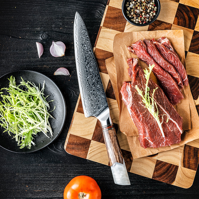 A chef using the rock-chopping motion with the Damara Kaku chef’s knife to finely mince herbs on a wooden cutting board.